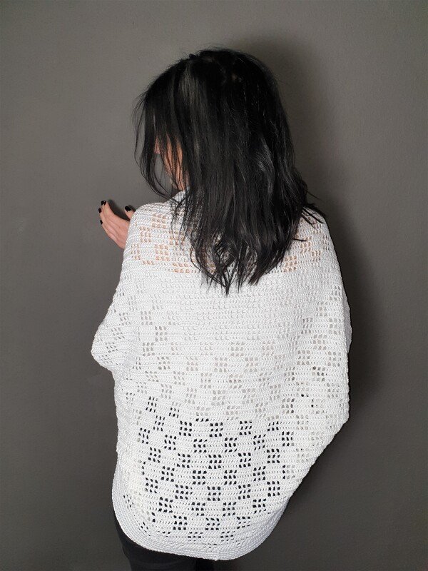 Rückansicht einer Person mit weißem gehäkeltem Seelenwärmer und feinem Lochmuster vor neutralem Hintergrund.
