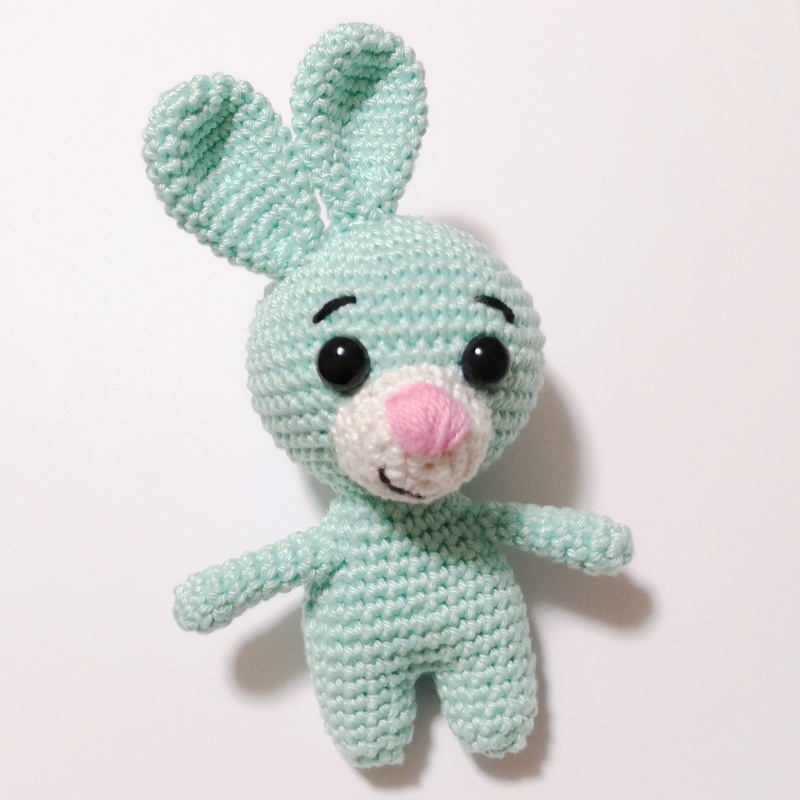 Nahaufnahme eines gehäkelten Amigurumi-Häschens in Mintgrün mit schwarzen Augen und rosa Nase auf weißem Hintergrund.