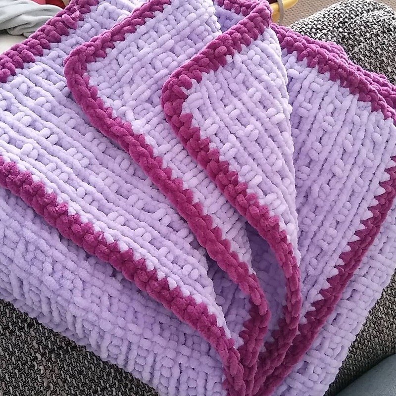 Gefaltete, grobgestrickte Babydecke in Flieder mit pinker Kante