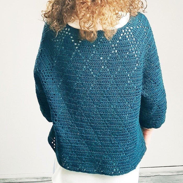 Back view of a woman wearing a teal crocheted sweater with a lacy yoke.