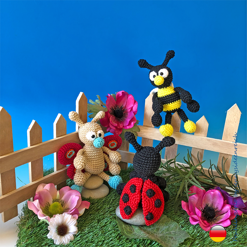 Gehäkelte Amigurumi-Figuren: Marienkäfer, Biene und Schmetterling neben Blumen und Holzzaun