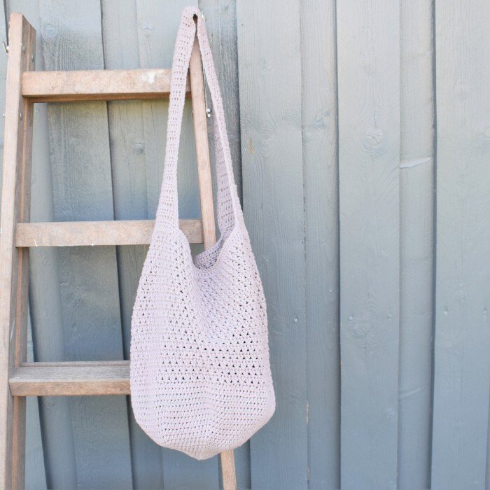 Light gray crocheted shopper bag hanging on a wooden ladder