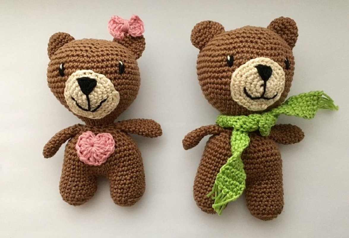 Zwei braune gehäkelte Amigurumi-Teddys, links mit rosa Herz und Schleife, rechts mit grünem Schal