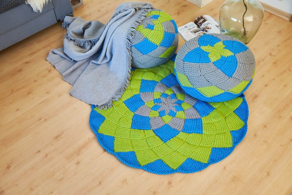 Gehäkelter runder Teppich und zwei passende Poufs in Blau, Grün und Grau auf hellem Holzboden