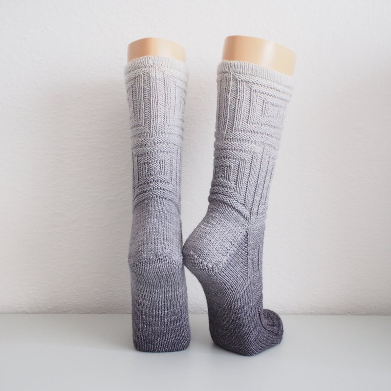 Pair of knitted gray gradient socks with geometric square pattern on mannequin legs.