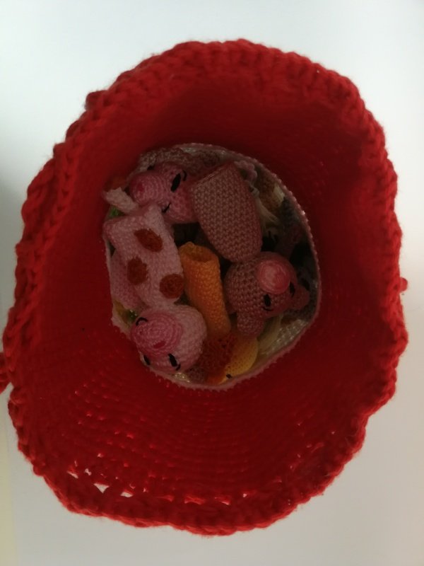 Blick in ein rotes gehäkeltes Körbchen mit mehreren kleinen Amigurumi-Handpuppen