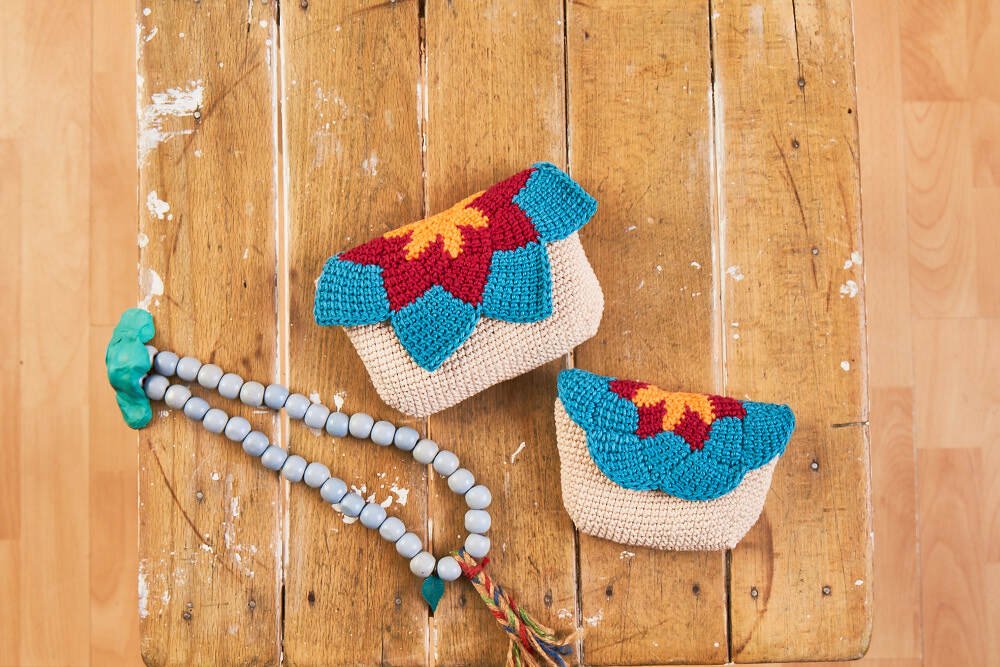 Zwei kleine gehäkelte Clutches mit buntem, muschelförmigem Klappenbesatz auf rustikalem Holztisch