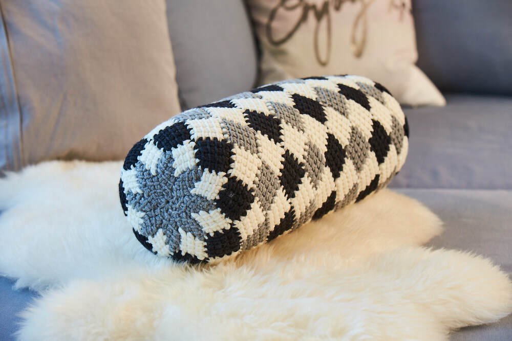 Gehäkelte zylindrische Kissenhülle mit schwarz-grau-wei
R.em geometrischem Muster auf Sofa