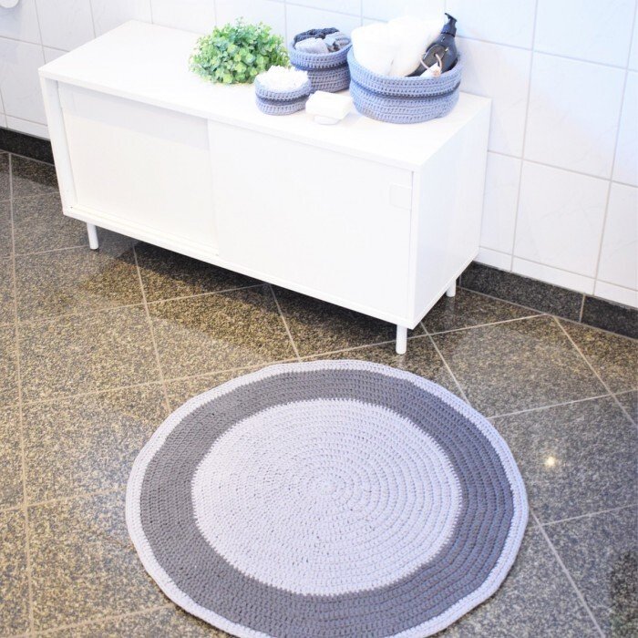 Round crocheted rug with light and dark grey concentric rings on a tiled bathroom floor
