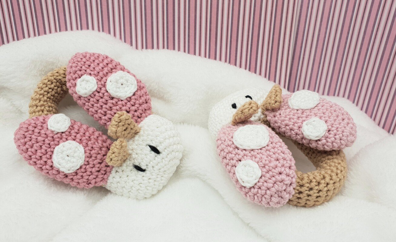 Zwei gehäkelte Marienkäfer-Greifringe (rosa, weiß, beige) auf weißer Decke