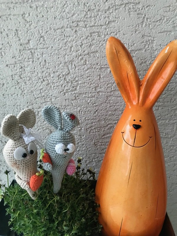 Kompakte gehäkelte Hasen mit Mini-Karotten neben großer orangefarbener Hasenfigur in einem Pflanztopf