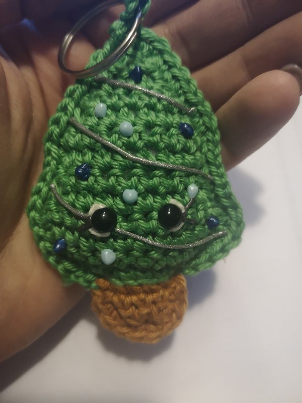 Gehäkelter grüner Weihnachtsbaum-Schlüsselanhänger mit farbigen Perlen, aufgestickten Augen und silbernen Girlanden in einer Hand
