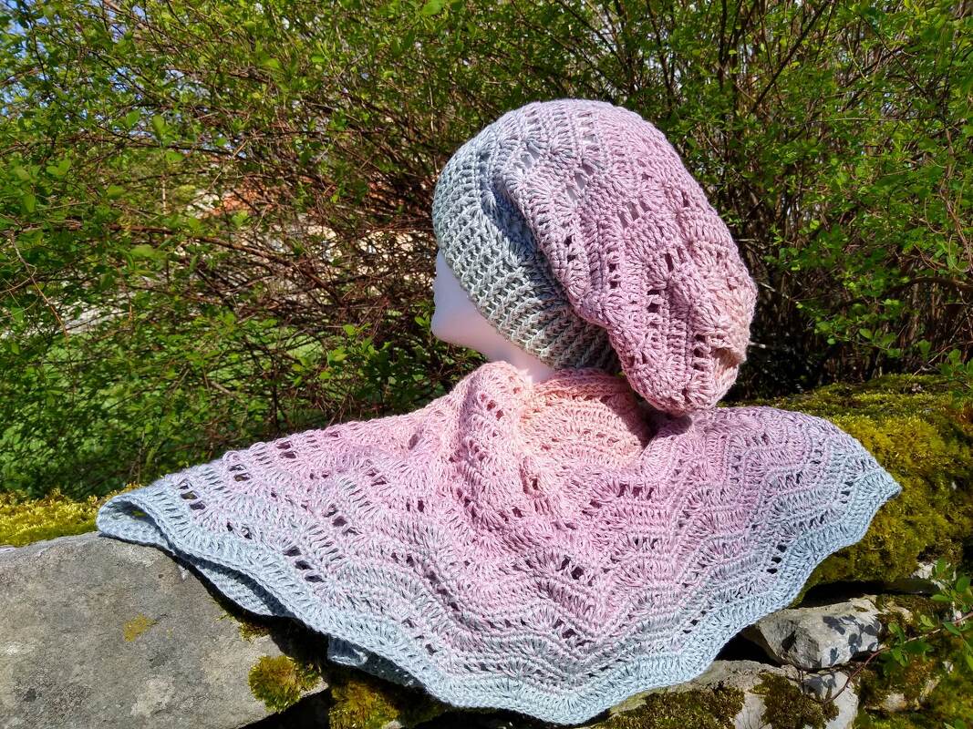 Mannequin mit gehäkelter Slouch-Mütze und passendem Dreieckstuch in Rosa-Grau Farbverlauf auf Steinmauer