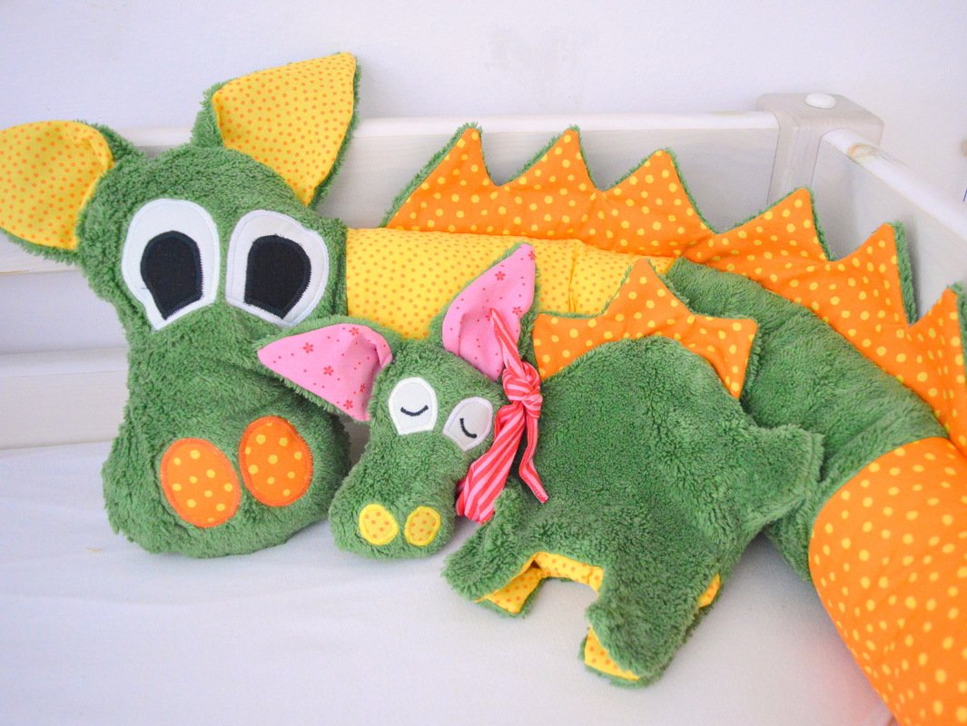 Grünes genähtes Drachenkissen und kleines Drachenstofftier mit applizierten Augen, rosa Ohren und orange-gelben gepunkteten Zacken