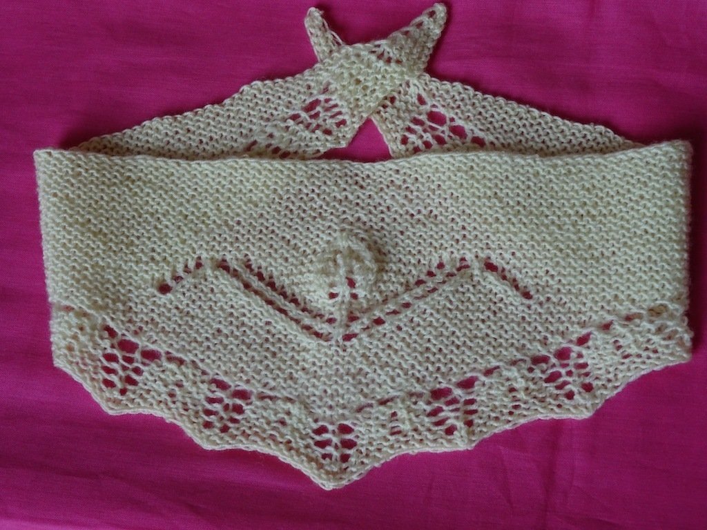 Cremefarbenes gestricktes Baby-Dreieckstuch mit Lochkante und Bändchen auf pinkem Hintergrund