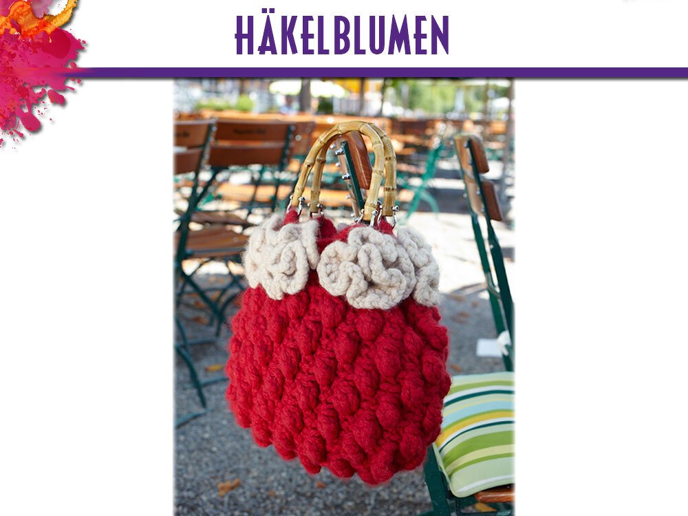 Rote gehäkelte Handtasche mit cremefarbenen Häkelblumen und Bambushenkeln, hängend an einem Stuhl im Freien.