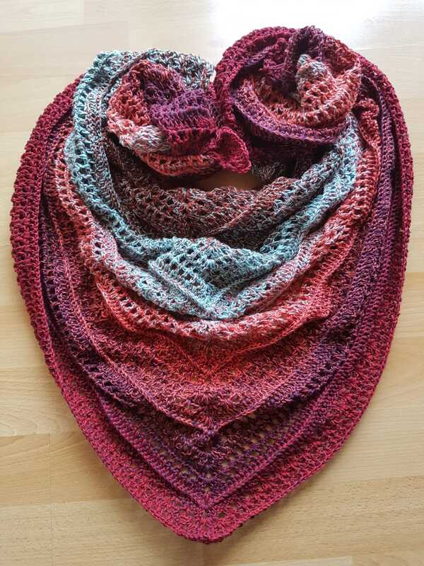 Gehäkeltes dreieckiges Tuch in roten, rosa und türkisfarbenen Verläufen auf hellem Holzboden