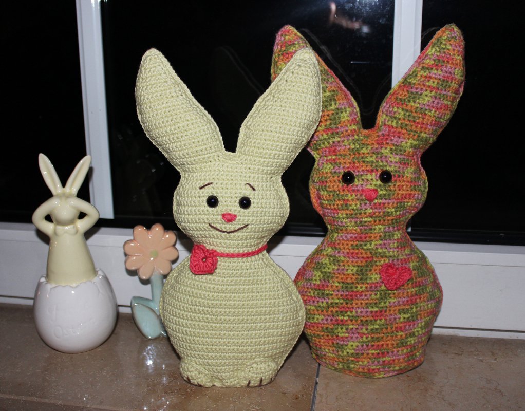 Zwei gehäkelte Amigurumi-Hasen (pastellgelb und meliert) auf Fensterbank mit Keramikdeko