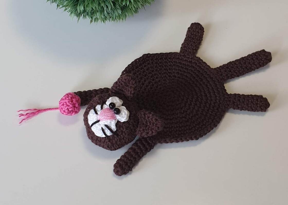 Gehäkelter brauner Katzen-Untersetzer mit rosa Nase und weißen Wangen auf hellem Untergrund