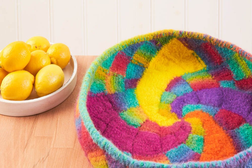 Bunter, flauschiger gehäkelter Aufbewahrungskorb mit Spiralmuster neben einer Schale mit Zitronen auf einer Holzfläche