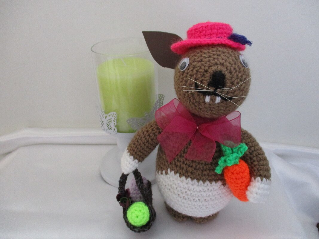 Brauner gehäkelter Amigurumi-Osterhase mit rosa Hut, Schleife, Möhre und kleinem Korb