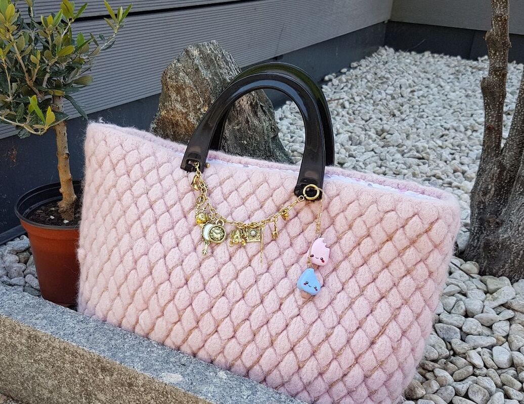 Gehäkelte und gefilzte rosa Tasche mit diamantförmigem Rautenmuster und schwarzen Henkeln