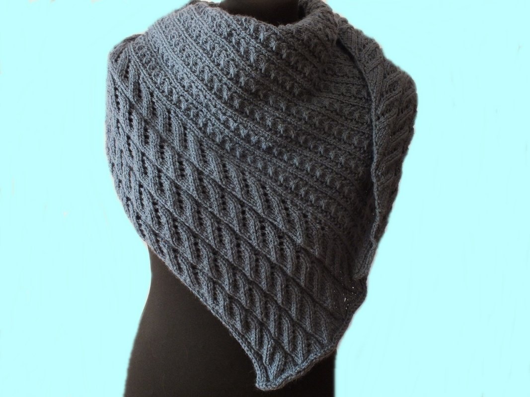 Grau-blaues gestricktes Dreieckstuch mit diagonalem Rauten- und Zopfmuster auf einer Schneiderpuppe.