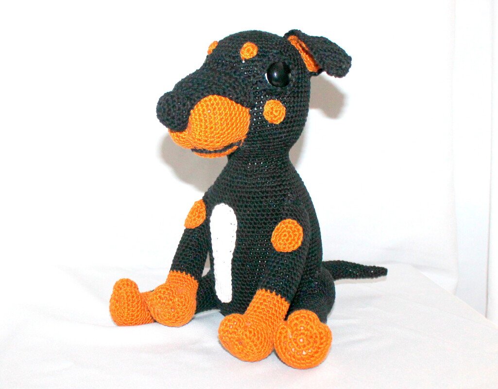 Gehäkelter sitzender Amigurumi‑Hund in Schwarz mit orangefarbenen Details und weißer Brust