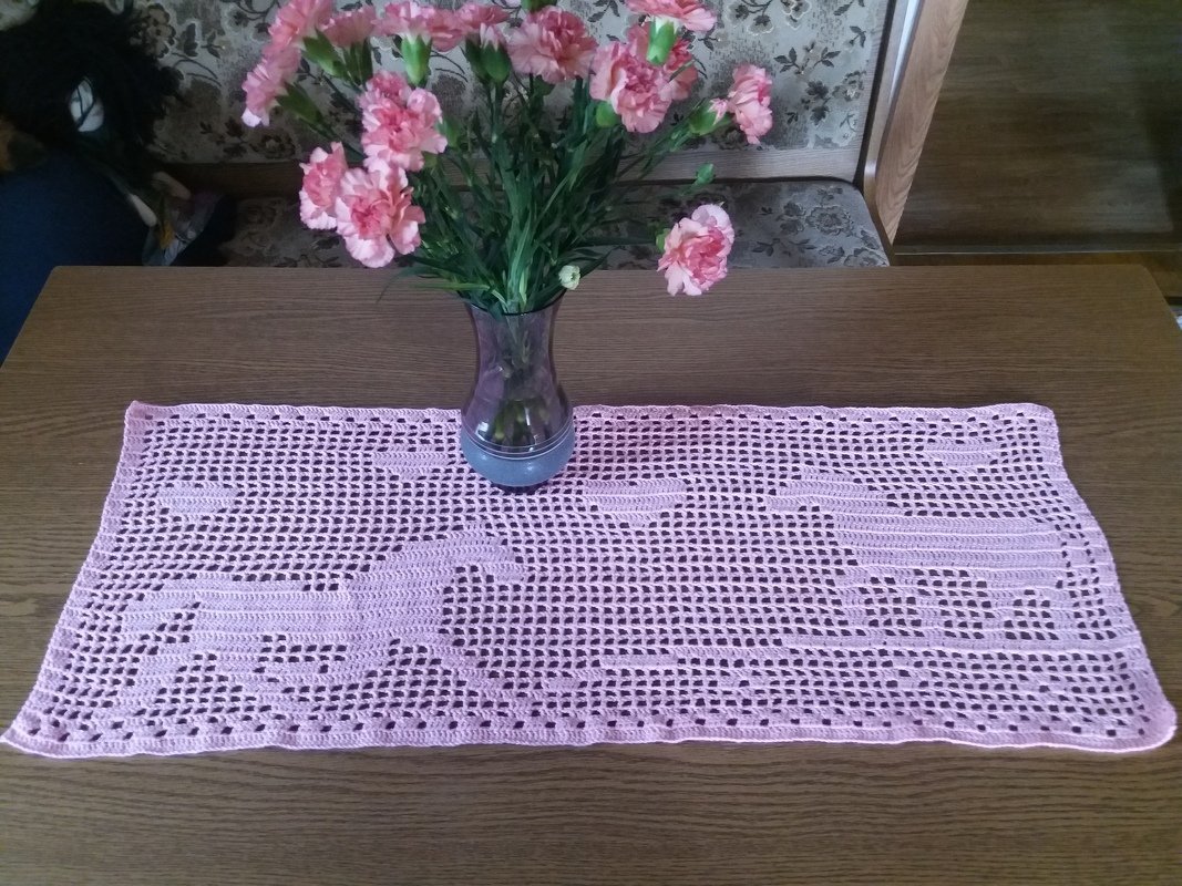Rosa-lila gehäkelter Tischläufer mit Pferdemustern und Vase mit rosa Nelken