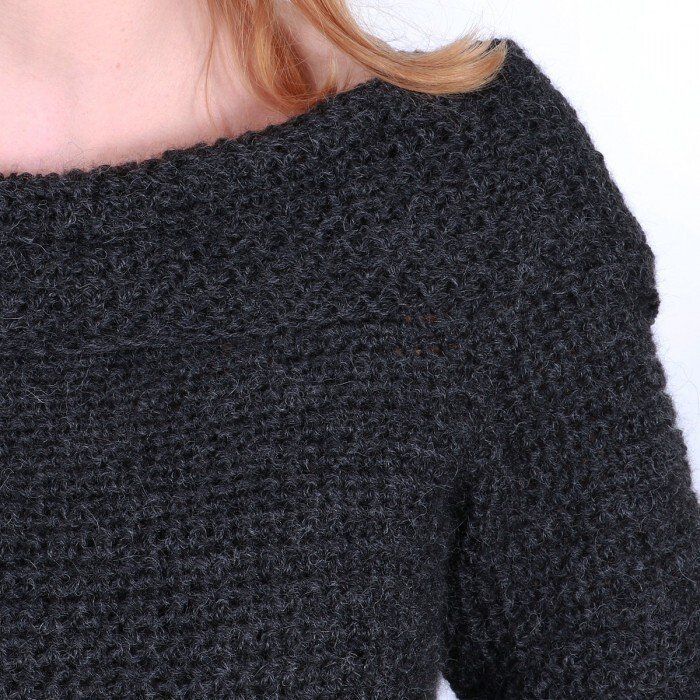 Close-up of a woman's shoulder and wide neckline in a dark gray crocheted sweater.