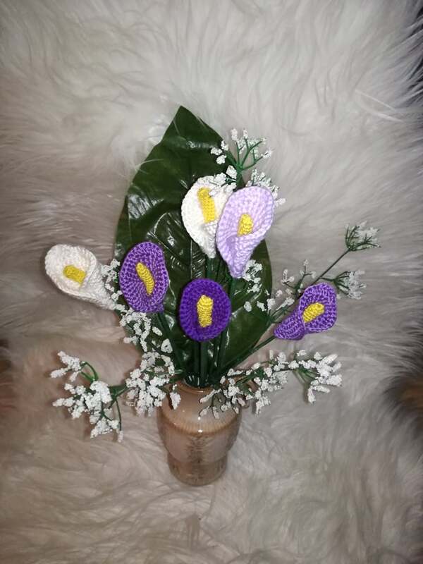 Vase mit gehäkelten Calla-Lilien in Weiß, Flieder und Lila, gelber Kolben, großes grünes Blatt und weiße Beiwerkzweige auf hellem Felluntergrund