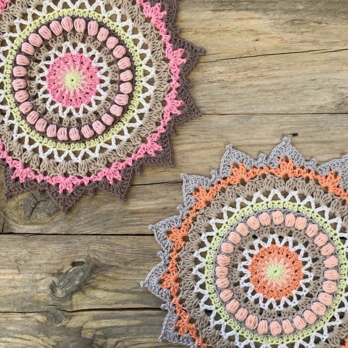 Zwei runde, gehäkelte Mandalas in Pastellfarben mit gezacktem Rand auf Holzuntergrund.