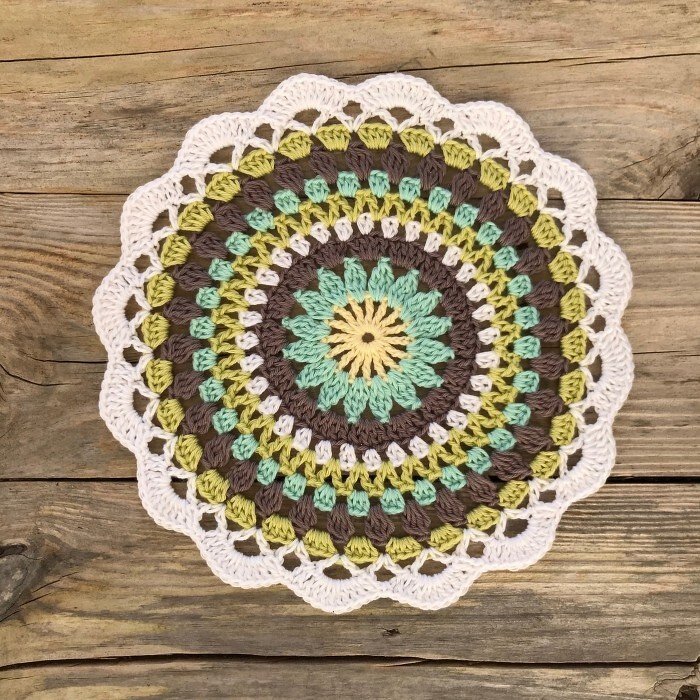 Round multicolored crocheted doily with scalloped edge on wooden planks