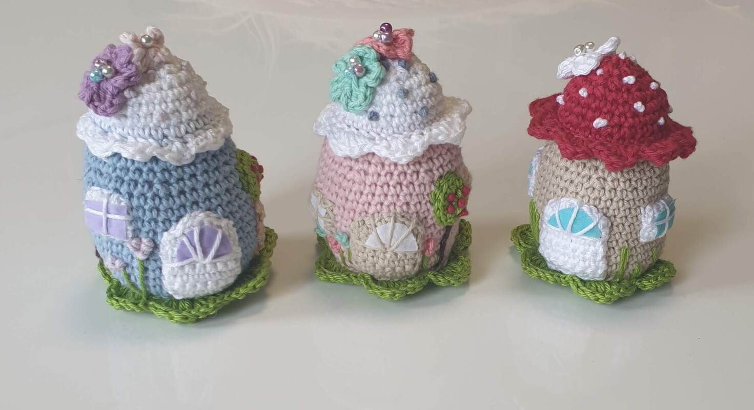 Drei gehäkelte Mini-Häuser in Pastell mit Blumen, Perlen und grünem Blattsockel