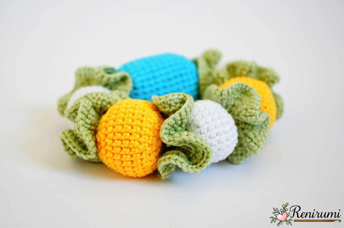 Yellow, blue and white crocheted balls with green ruffled edges on a white background