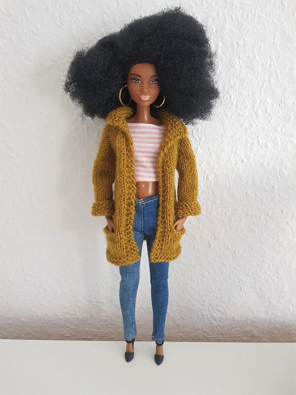 Puppe mit senfgelber gestrickter Cardigan, gestreiftem Croptop und blauer Jeans vor heller Wand
