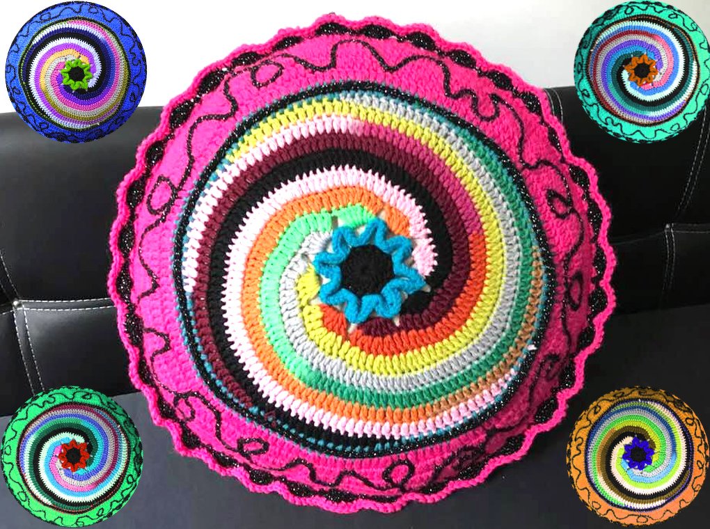 Rundes gehäkeltes Kissen mit buntem Spiralmuster und pinker Umrandung auf dunklem Sofa.