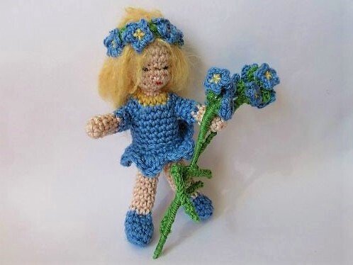 Kleine gehäkelte Puppe mit angenähtem Haar, gesticktem Gesicht und gehäkelten Blüten