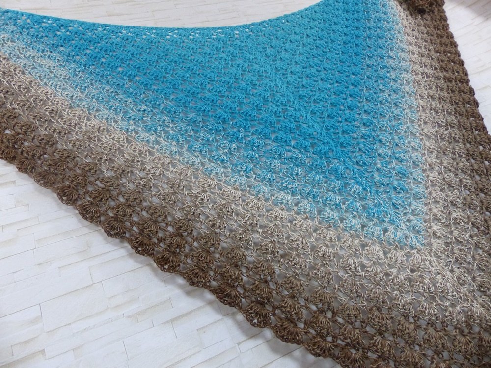 Gehäkeltes Dreieckstuch mit türkisem zu braunem Farbverlauf und Muschelkante auf hellem Untergrund
