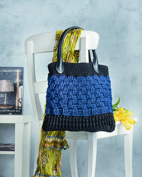 Gehäkelte Henkeltasche in Blau und Schwarz mit Strukturmuster, auf einem weißen Stuhl