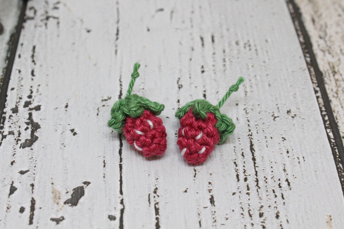 Zwei kleine gehäkelte Erdbeeren mit grünen Kelchblättern auf weißer Holzoberfläche