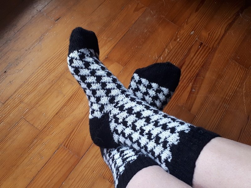 Gestrickte schwarz-weiße Socken mit Hahnentrittmuster auf Holzboden.