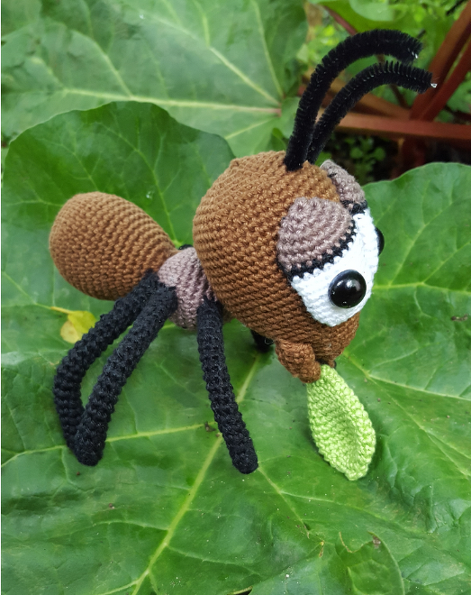 Gehäkelte Amigurumi-Ameise in Braun mit schwarzen Beinen, Fühlern und grünem Blatt