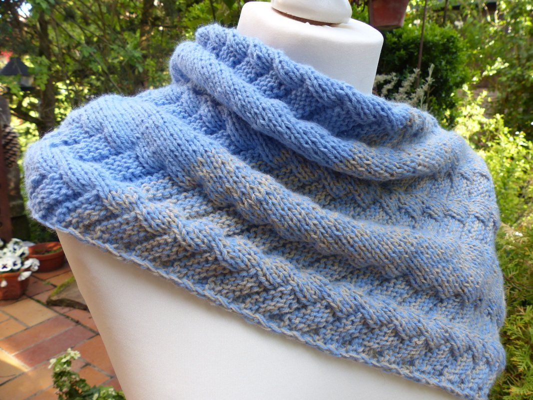 Gestrickter Schal in Blautönen mit beigen Sprenkeln und deutlich sichtbarem Texturmuster, präsentiert im Freien.