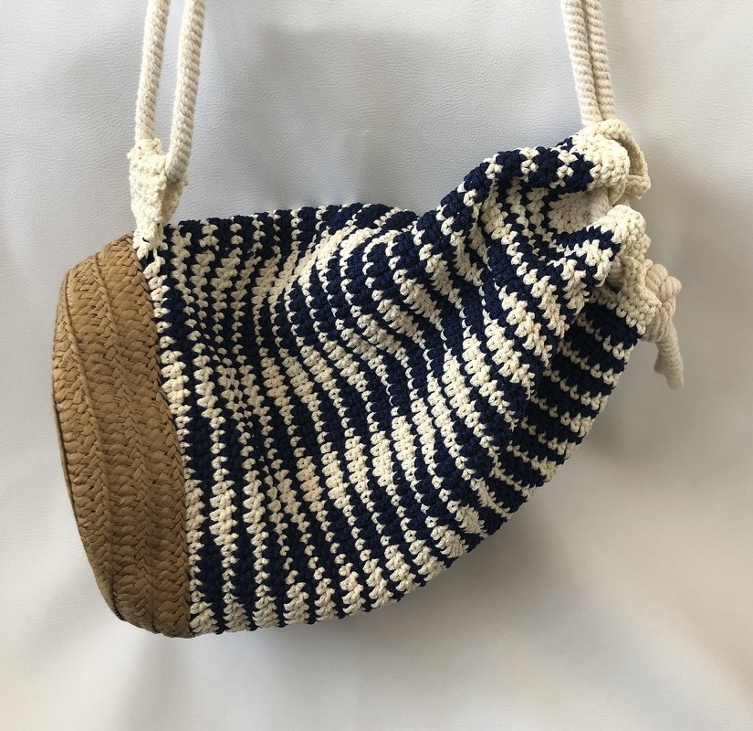 Gehäkelte Beuteltasche in Dunkelblau und Creme mit geflochtenem Bastboden und Seilkordelzug.