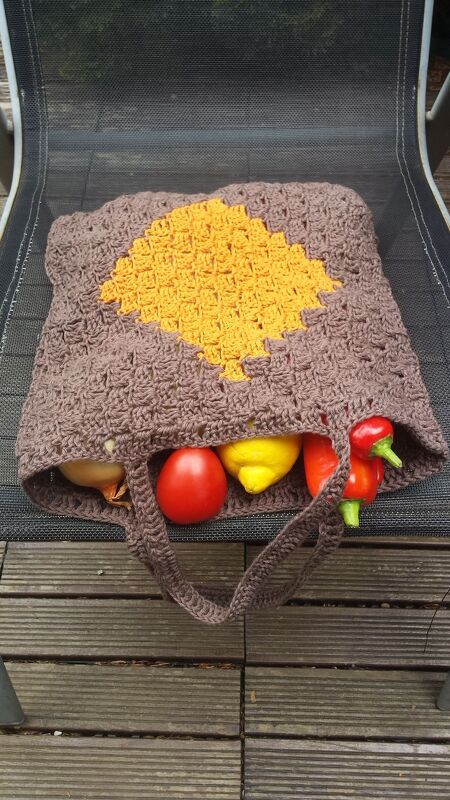 Gehäkelte braune Henkeltasche mit gelber Raute, gefüllt mit Tomate, Zitrone, Paprika und Zwiebel
