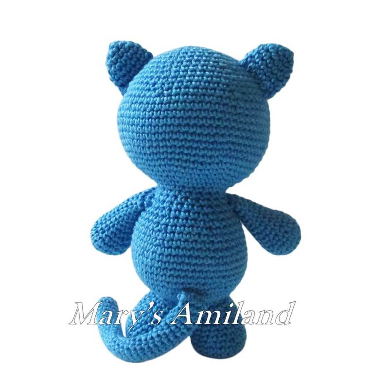 Back view of a blue crocheted amigurumi cat with curled tail and rounded ears on a white background.