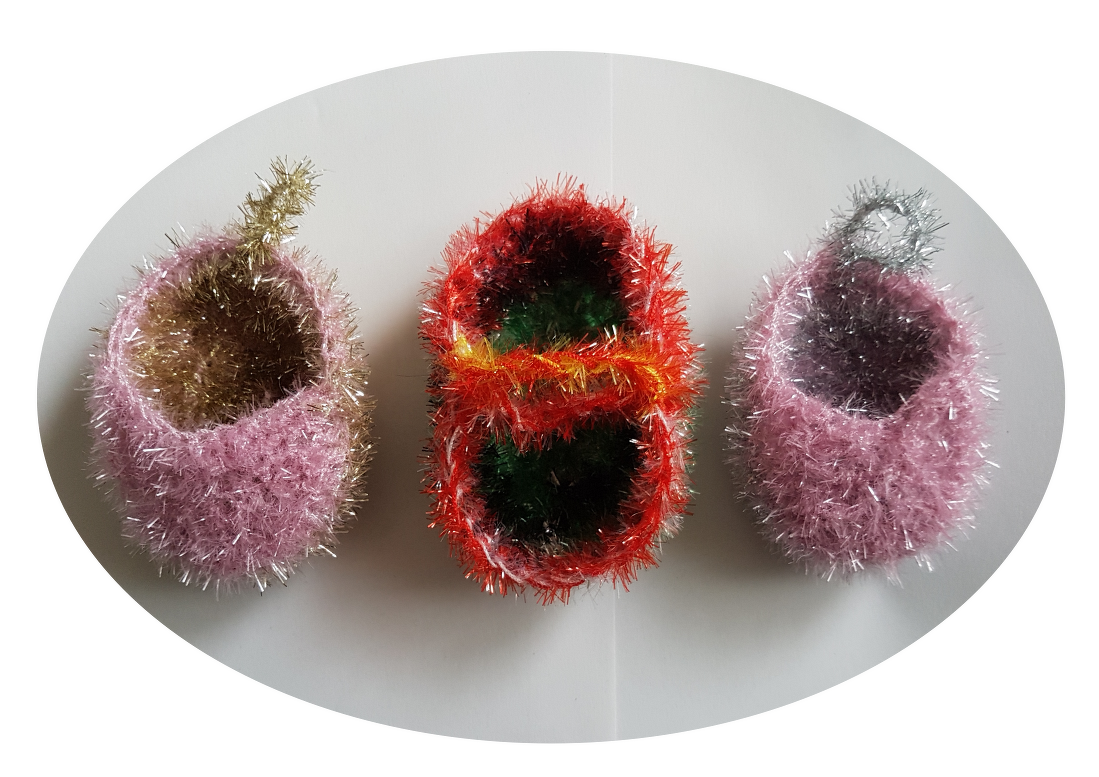 Drei funkelnde, gehäkelte Körbchen in Rosa-Gold, Rot-Grün und Rosa-Silber aus metallisch schimmernden Fäden, nebeneinander auf hellem Untergrund