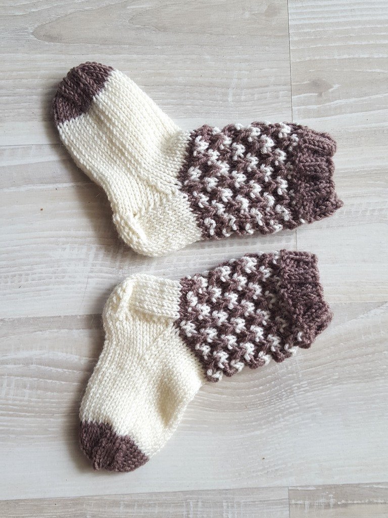 Zweifarbig gestrickte Babysocken in Creme und Braun, flach liegend