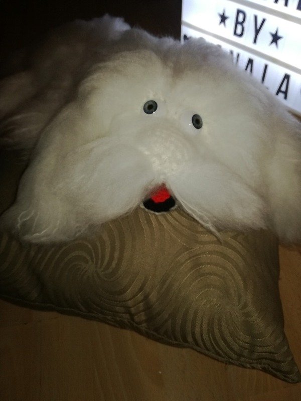 Weißes flauschiges Amigurumi in Drachenform mit Knopfaugen, buschigem Schnurrbart und roter Zunge